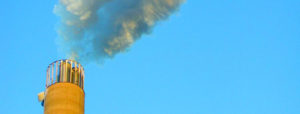 Daytime view of emissions leaving a smoke stack under a blue sky