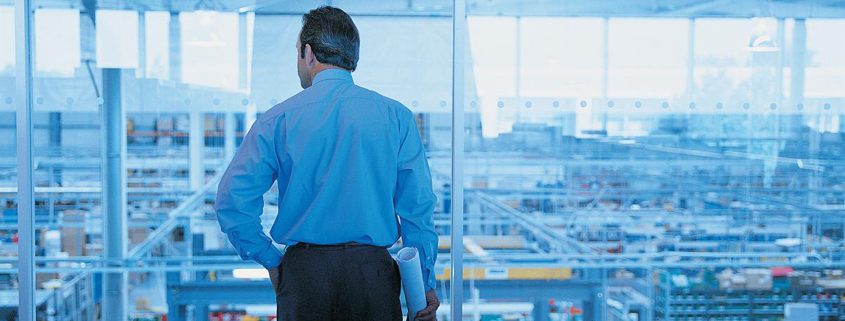 Interior view of an executive in a glass-walled office looking out over a factory floor