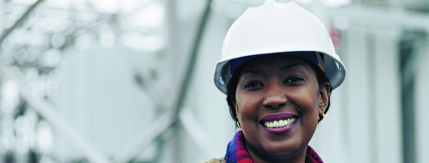 Daytime portrait of a smiling black woman in a hard hat working at an energy facility