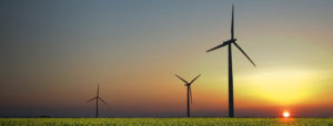 View of three wind turbines in silhouette as the sun rises over a flat, green field