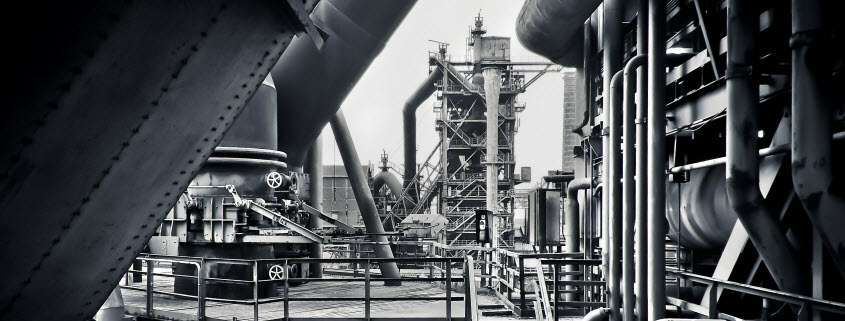 Black and white image of an industrial plant as seen from a catwalk, with extensive piping visible on all sides
